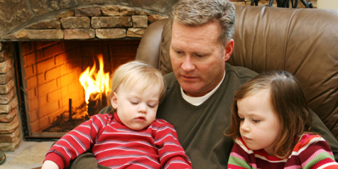 Man and two children sitting in front of flaming fireplace